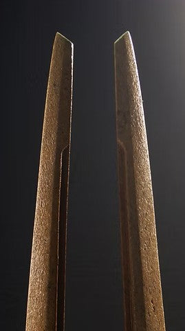 Tall Purbeck stone sculpture with a central vertical opening and tapered peak, standing on a black granite base, showing fossil textures and carved geometry against a dark background.