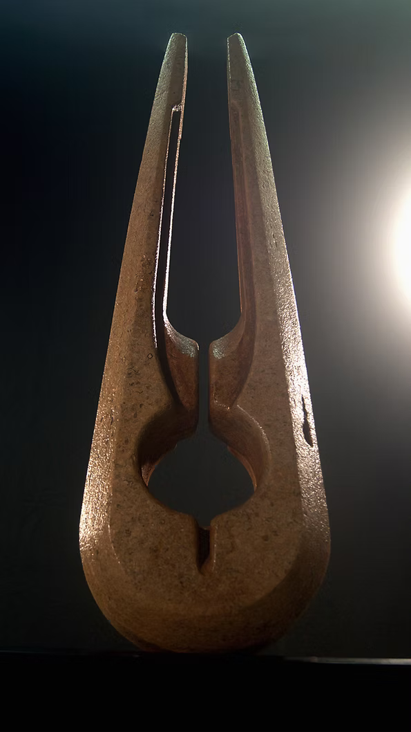 Tall Purbeck stone sculpture with a central vertical opening and tapered peak, standing on a black granite base, showing fossil textures and carved geometry against a dark background.