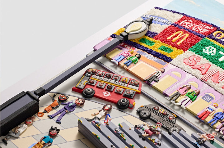 A vibrant, three-dimensional polymer clay artwork of Piccadilly Circus, featuring the iconic curved billboard with brands like Coca-Cola, McDonald’s, and TDK rendered in colourful textured beads. The street scene below includes a classic red double-decker bus marked “38 Piccadilly Circus,” a London black cab, and crowds of joyful figures in bright handmade outfits. Sculpted pigeons dot the grey stone steps beneath the Shaftesbury Memorial Fountain with a golden winged Eros above. 