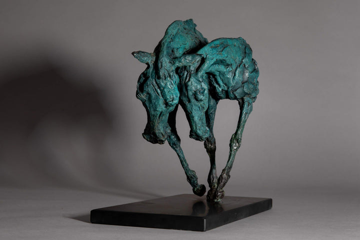 Bronze sculpture of two intertwined horse heads with elongated ears, rendered in a turquoise verdigris finish, symbolising love and hope, mounted on a slate base.