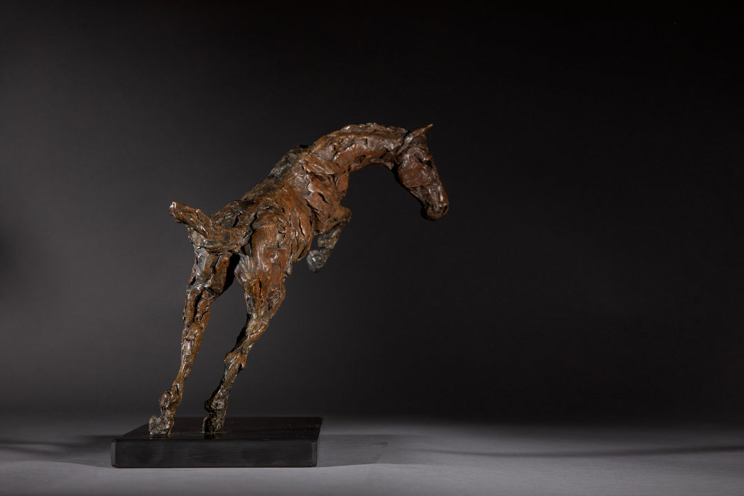 Bronze sculpture of a powerful jumping horse titled Loving Life (Hunter), captured mid-leap with expressive musculature and dynamic energy, mounted on a dark oval base and photographed against a neutral backdrop.