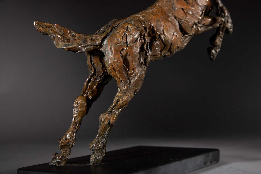 Bronze sculpture of a powerful jumping horse titled Loving Life (Hunter), captured mid-leap with expressive musculature and dynamic energy, mounted on a dark oval base and photographed against a neutral backdrop.