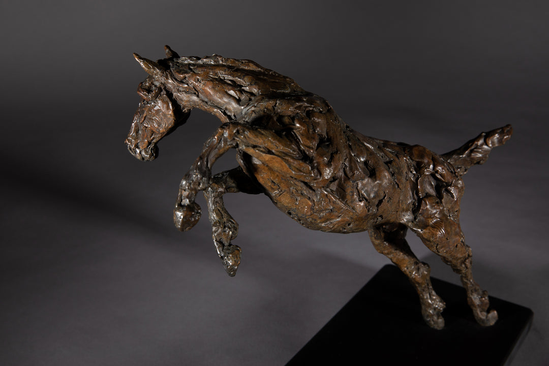 Bronze sculpture of a powerful jumping horse titled Loving Life (Hunter), captured mid-leap with expressive musculature and dynamic energy, mounted on a dark oval base and photographed against a neutral backdrop.