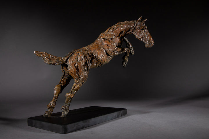 Bronze sculpture of a powerful jumping horse titled Loving Life (Hunter), captured mid-leap with expressive musculature and dynamic energy, mounted on a dark oval base and photographed against a neutral backdrop.