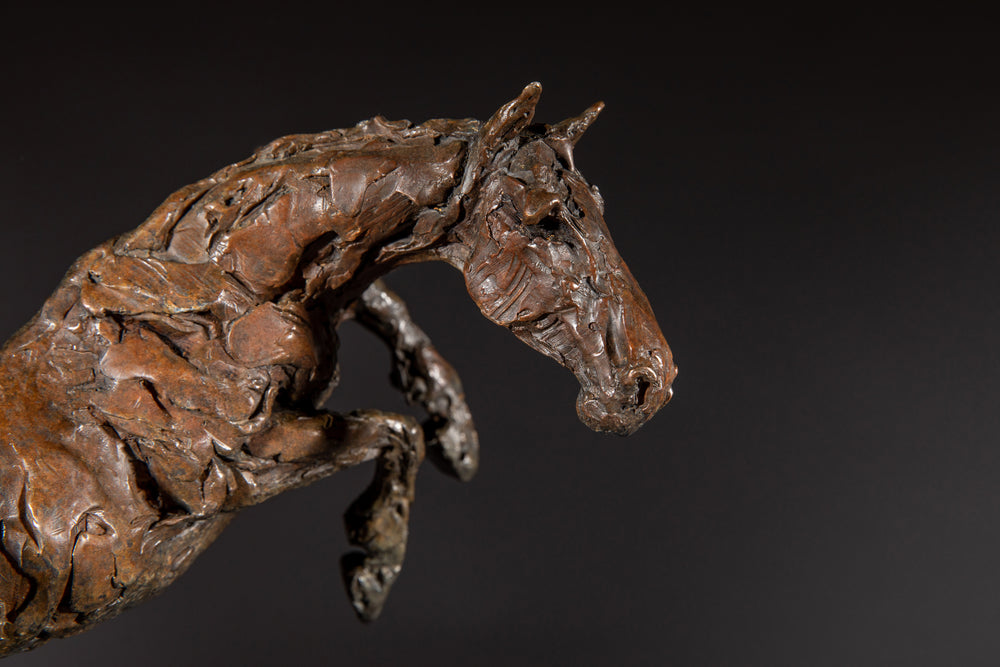 Bronze sculpture of a powerful jumping horse titled Loving Life (Hunter), captured mid-leap with expressive musculature and dynamic energy, mounted on a dark oval base and photographed against a neutral backdrop.
