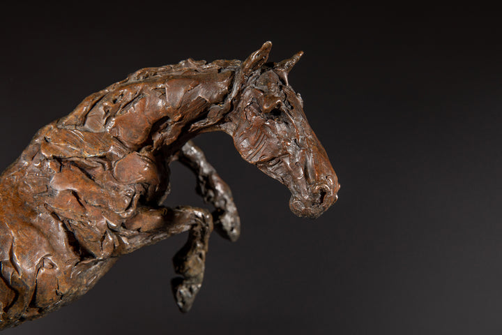 Bronze sculpture of a powerful jumping horse titled Loving Life (Hunter), captured mid-leap with expressive musculature and dynamic energy, mounted on a dark oval base and photographed against a neutral backdrop.