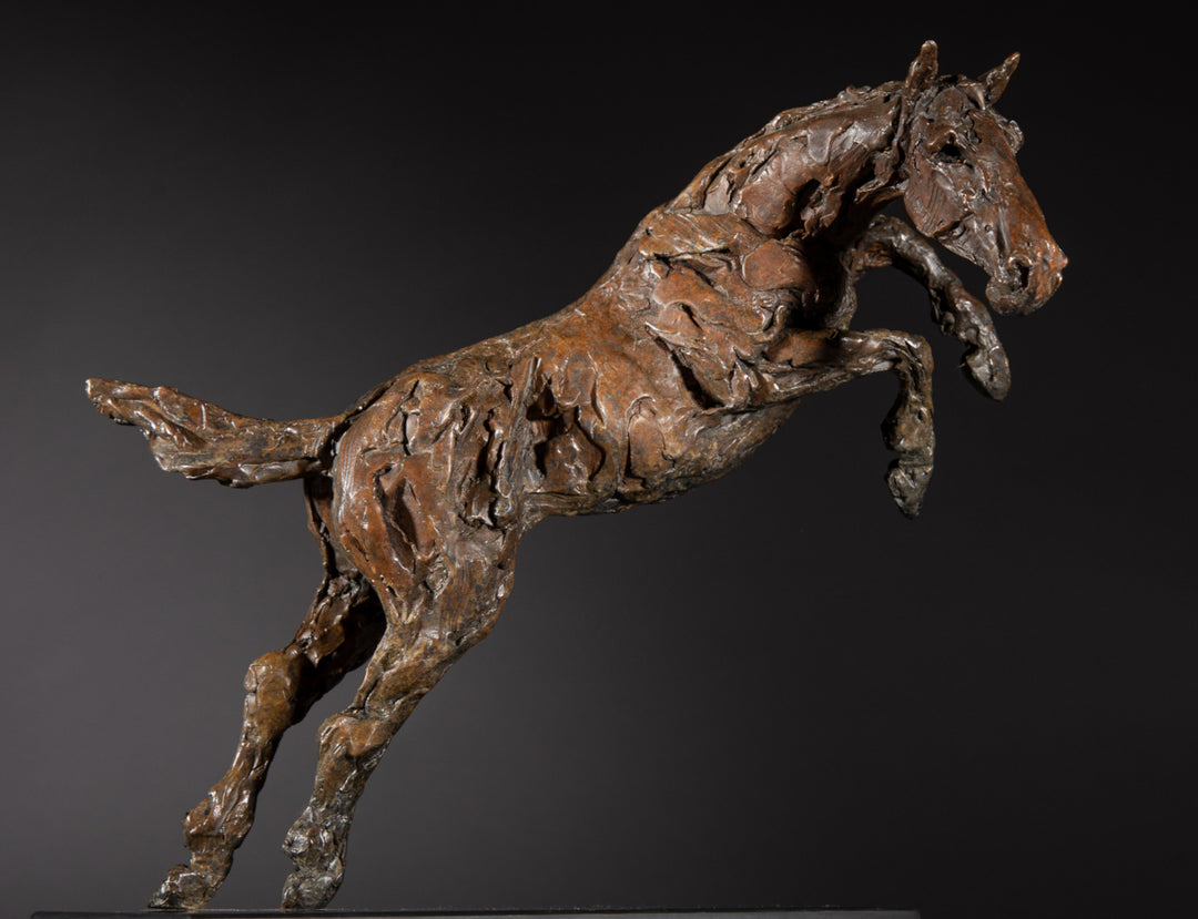 Bronze sculpture of a powerful jumping horse titled Loving Life (Hunter), captured mid-leap with expressive musculature and dynamic energy, mounted on a dark oval base and photographed against a neutral backdrop.