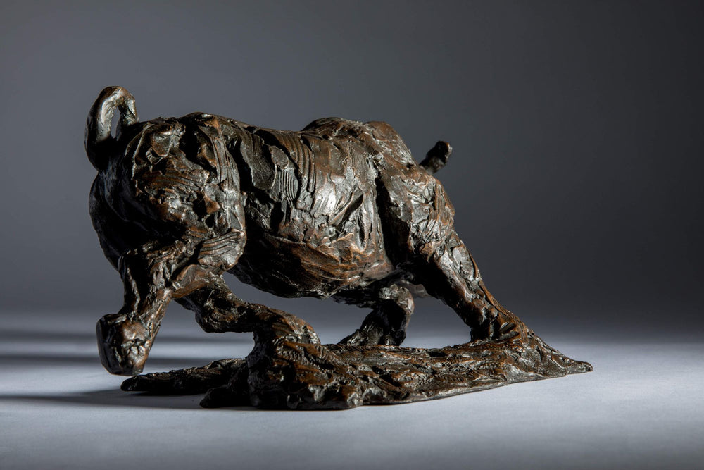 Bronze sculpture of a white rhino mid-charge, captured with bold textures and muscular form, evoking movement and strength.
