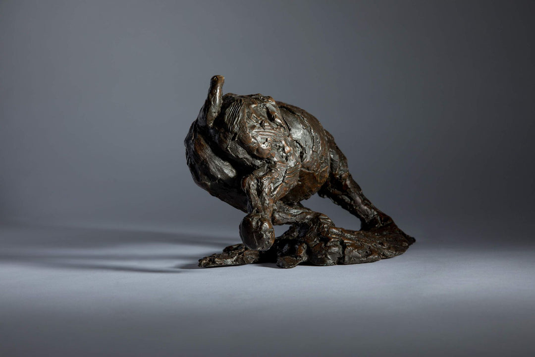 Bronze sculpture of a white rhino mid-charge, captured with bold textures and muscular form, evoking movement and strength.