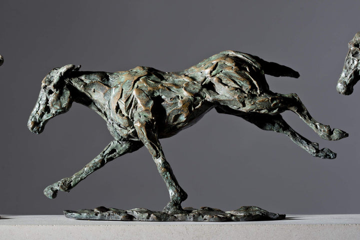 Bronze sculpture of three galloping horses mounted on a Portland stone base, capturing the fluid motion and changing form of equine movement in a verdigris finish.