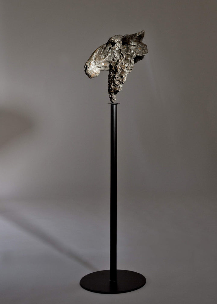 Life-size bronze sculpture of a sheep’s head with textured fleece and alert, characterful expression, mounted on a tall dark metal stand.