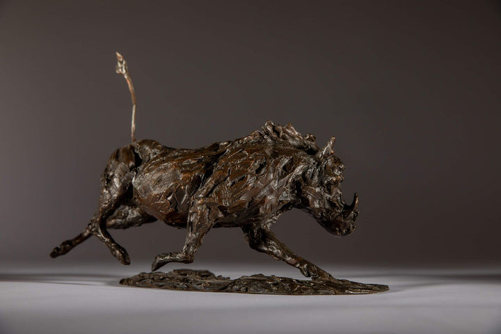 Bronze sculpture of a warthog mid-sprint with exaggerated texture and raised tail, captured in dynamic motion and set against a neutral backdrop.