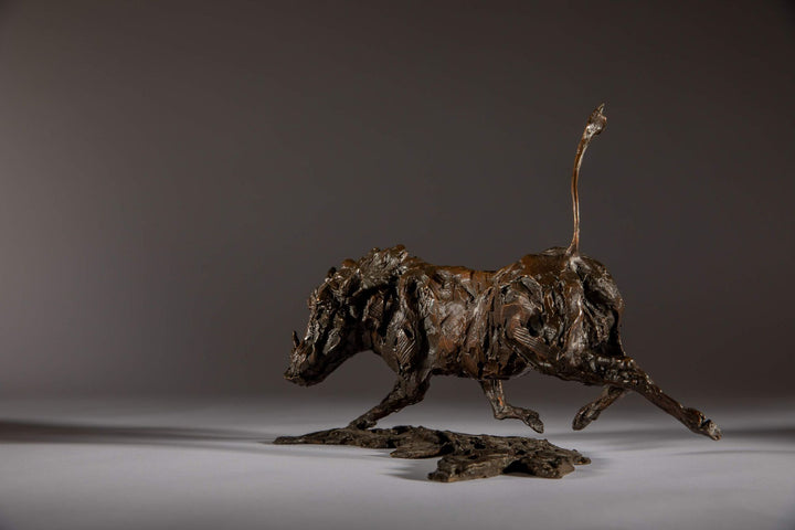 Bronze sculpture of a warthog mid-sprint with exaggerated texture and raised tail, captured in dynamic motion and set against a neutral backdrop.