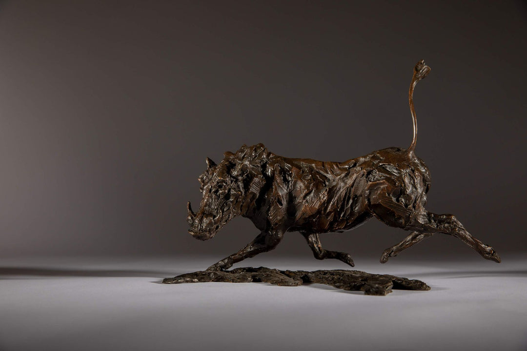 Bronze sculpture of a warthog mid-sprint with exaggerated texture and raised tail, captured in dynamic motion and set against a neutral backdrop.