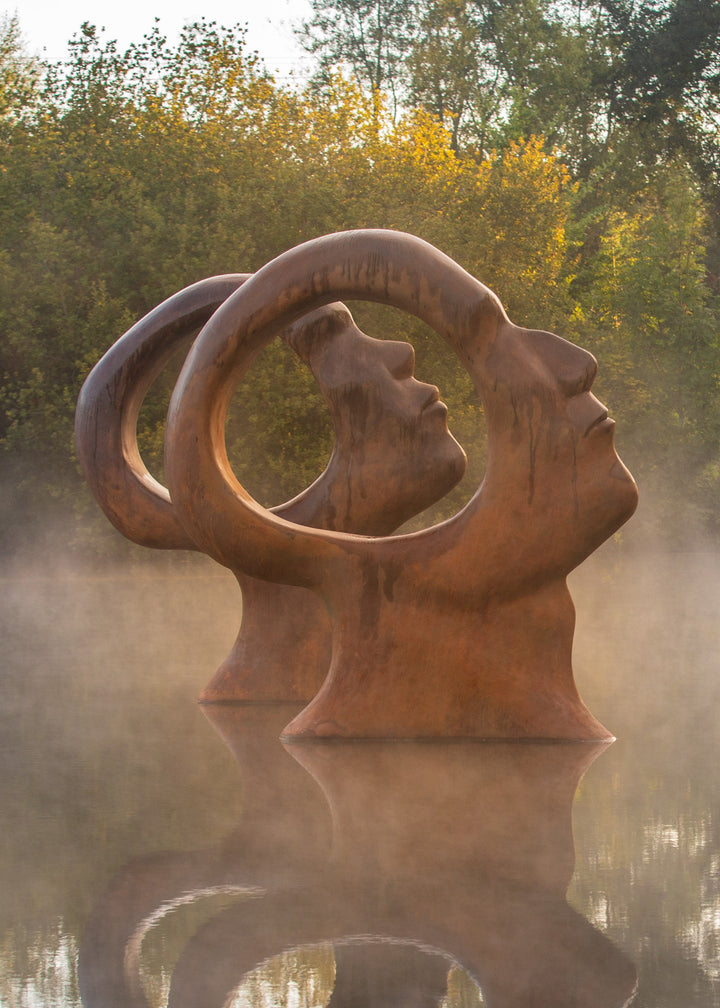 Simon Gudgeon bronze sculpture Search for Enlightenment featuring monumental interlocking abstract human forms with circular openings displayed within a landscaped outdoor setting.