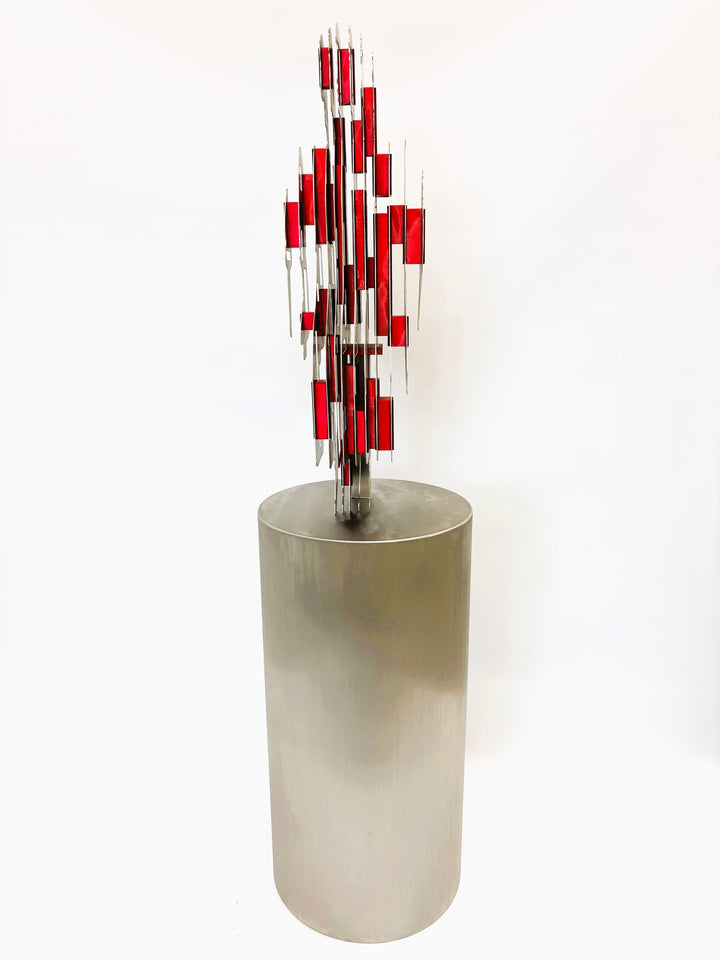 Sculpture titled Seated Girl I by Tom Hiscox, composed of layered stainless steel with red resin inserts forming a stylised seated female figure, shown from multiple angles on a brushed circular base.