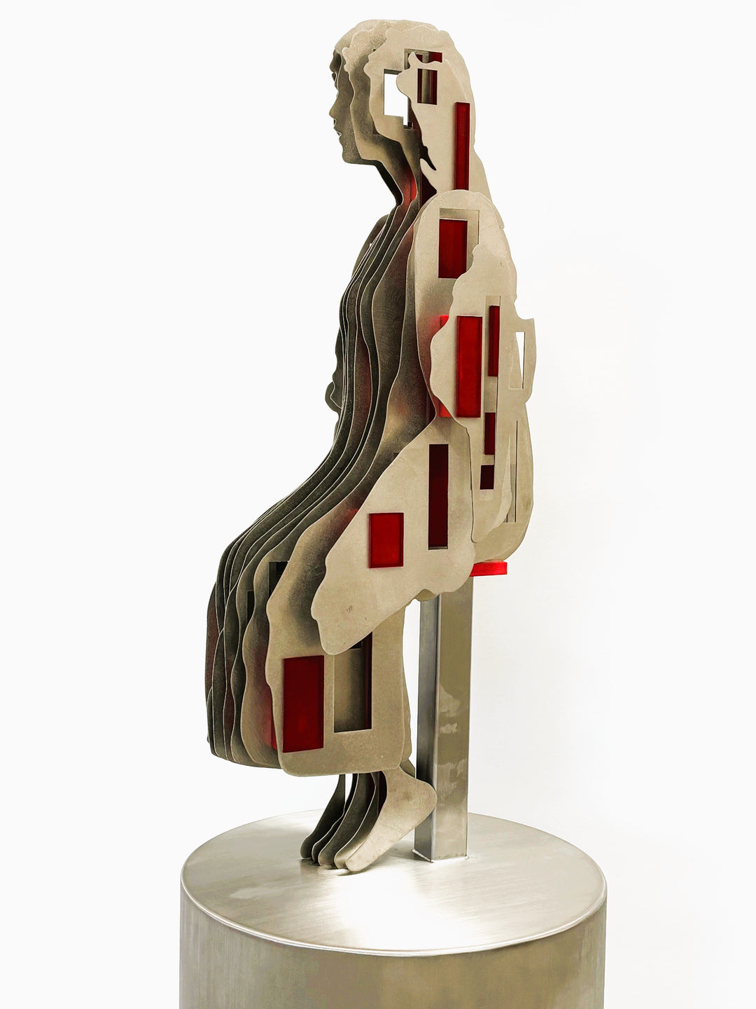 Sculpture titled Seated Girl I by Tom Hiscox, composed of layered stainless steel with red resin inserts forming a stylised seated female figure, shown from multiple angles on a brushed circular base.