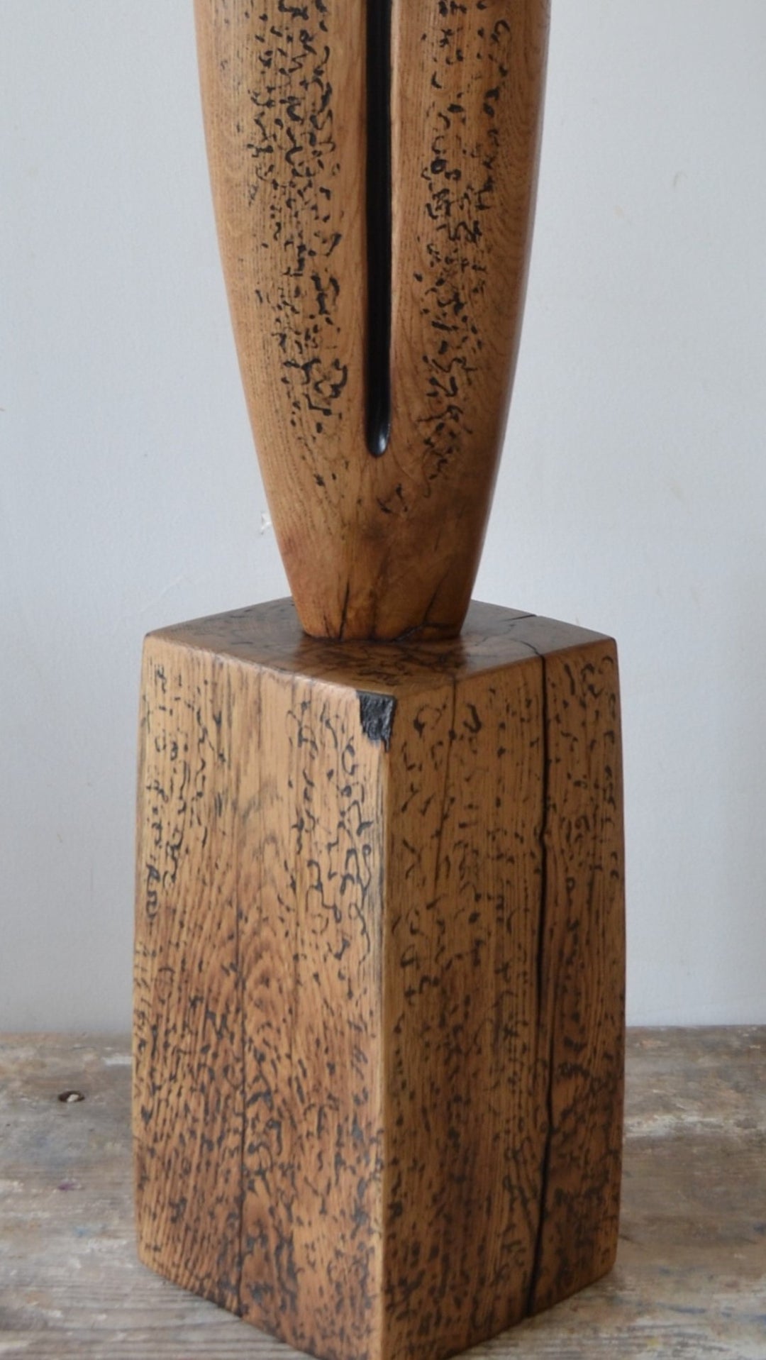 Sentinel by Nicola Beattie – tall, hand-carved oak sculpture with a smooth tapering profile and deep central black inlay ending in a keyhole opening. Warm beige oak with blackened markings and natural cracks, echoing ancient standing stones in a minimalist, monumental style.