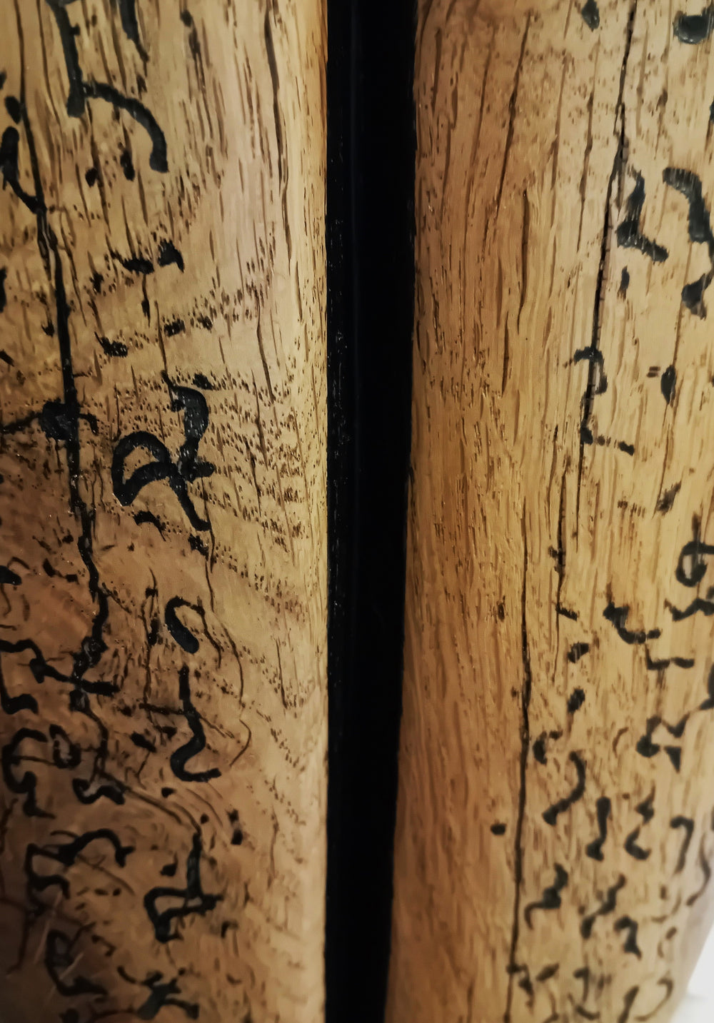 Sentinel by Nicola Beattie – tall, hand-carved oak sculpture with a smooth tapering profile and deep central black inlay ending in a keyhole opening. Warm beige oak with blackened markings and natural cracks, echoing ancient standing stones in a minimalist, monumental style.