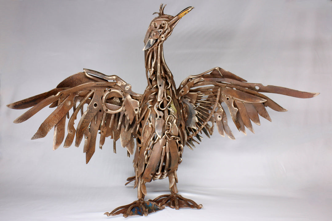 ‘Shag’ sculpture, full-size seabird crafted entirely from reclaimed vintage metal hand tools, with wings spread wide and intricate detailing in chains, spanners, blades, and pliers. The industrial bronze-brown patina enhances the bird’s strength and character, transforming utilitarian objects into a powerful work of contemporary recycled art.