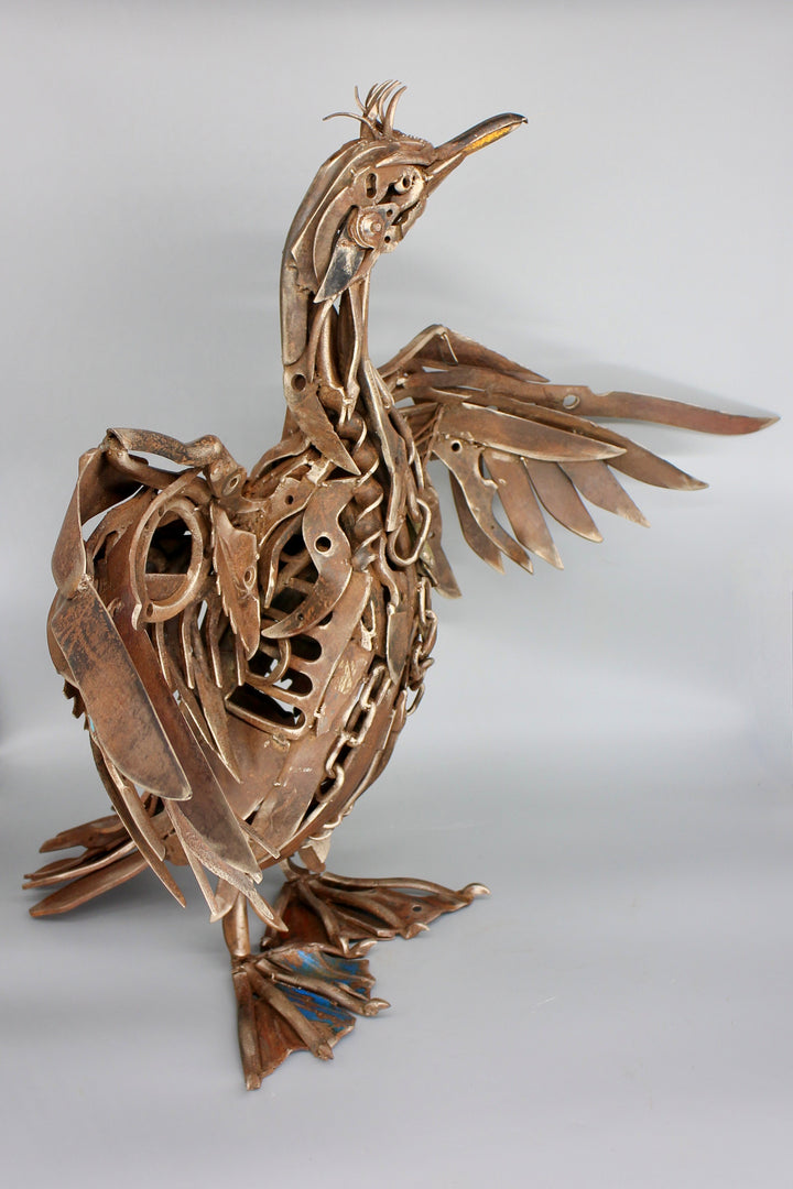 ‘Shag’ sculpture, full-size seabird crafted entirely from reclaimed vintage metal hand tools, with wings spread wide and intricate detailing in chains, spanners, blades, and pliers. The industrial bronze-brown patina enhances the bird’s strength and character, transforming utilitarian objects into a powerful work of contemporary recycled art.