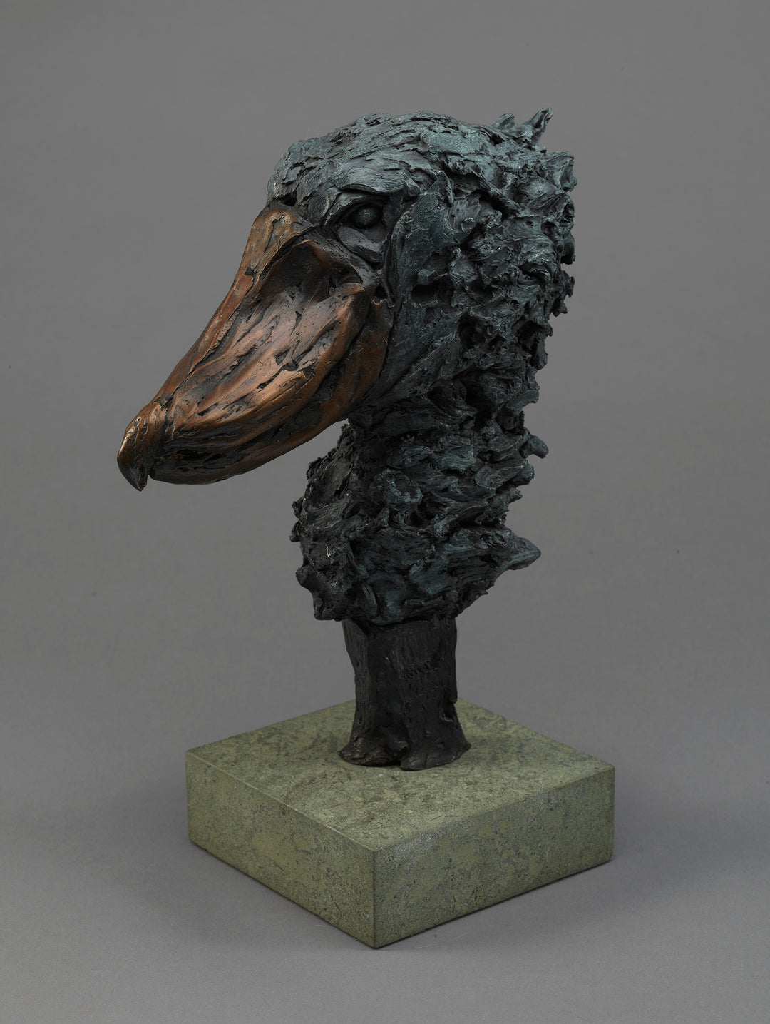 Bronze sculpture of a shoebill head with heavily textured feathers and a smooth, oversized beak, mounted on a stone base