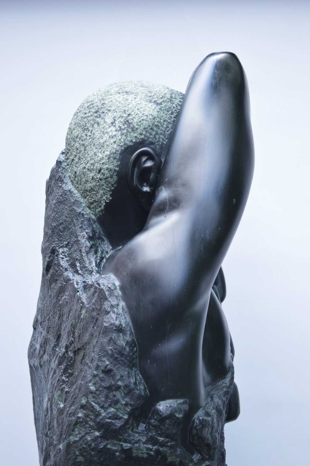 Deborah Harrison sculpture Slave Song, a one-off hand-carved black soapstone figure showing a bound male form with shackled wrist and heavy chain links, emerging from raw stone. The polished dark surface contrasts against the rough, natural texture, creating a powerful narrative of struggle, endurance, and the human spirit.
