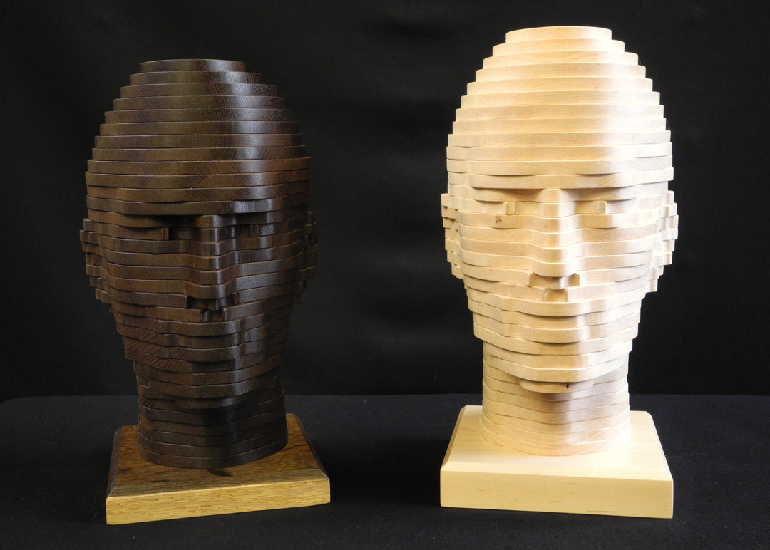Sliced Heads by Max McCance, one-off layered wood sculptures in maple and fumed oak, forming two stylised busts with hand-shaped strata that reveal masculine and feminine features through geometric abstraction.