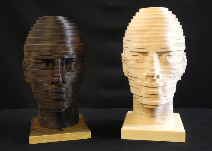 Sliced Heads by Max McCance, one-off layered wood sculptures in maple and fumed oak, forming two stylised busts with hand-shaped strata that reveal masculine and feminine features through geometric abstraction.