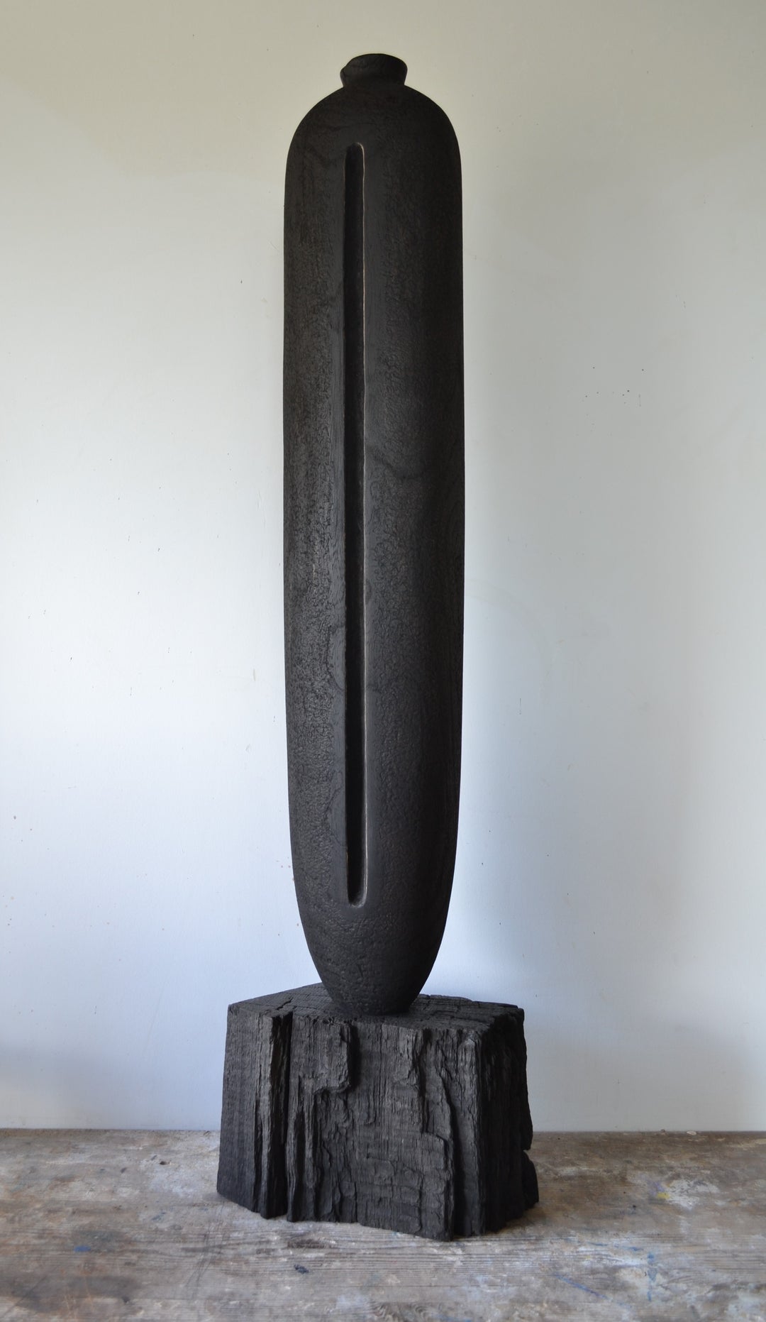 Solitude by Nicola Beattie – tall hand-carved sculpture in charred sycamore and bog oak, with elongated vertical form, deep central recess, and textured blackened surface on rugged base, evoking ancient standing stones and quiet resilience.
