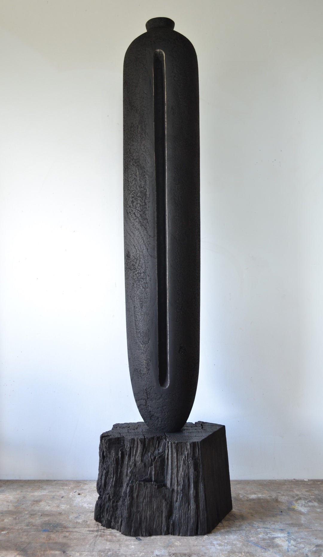 Solitude by Nicola Beattie – tall hand-carved sculpture in charred sycamore and bog oak, with elongated vertical form, deep central recess, and textured blackened surface on rugged base, evoking ancient standing stones and quiet resilience.