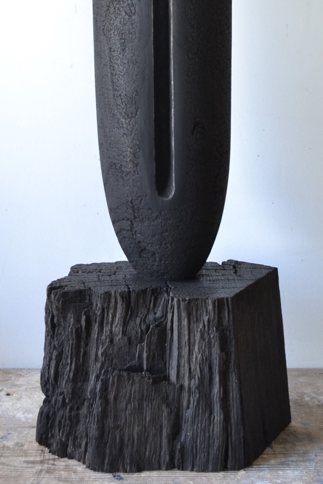 Solitude by Nicola Beattie – tall hand-carved sculpture in charred sycamore and bog oak, with elongated vertical form, deep central recess, and textured blackened surface on rugged base, evoking ancient standing stones and quiet resilience.