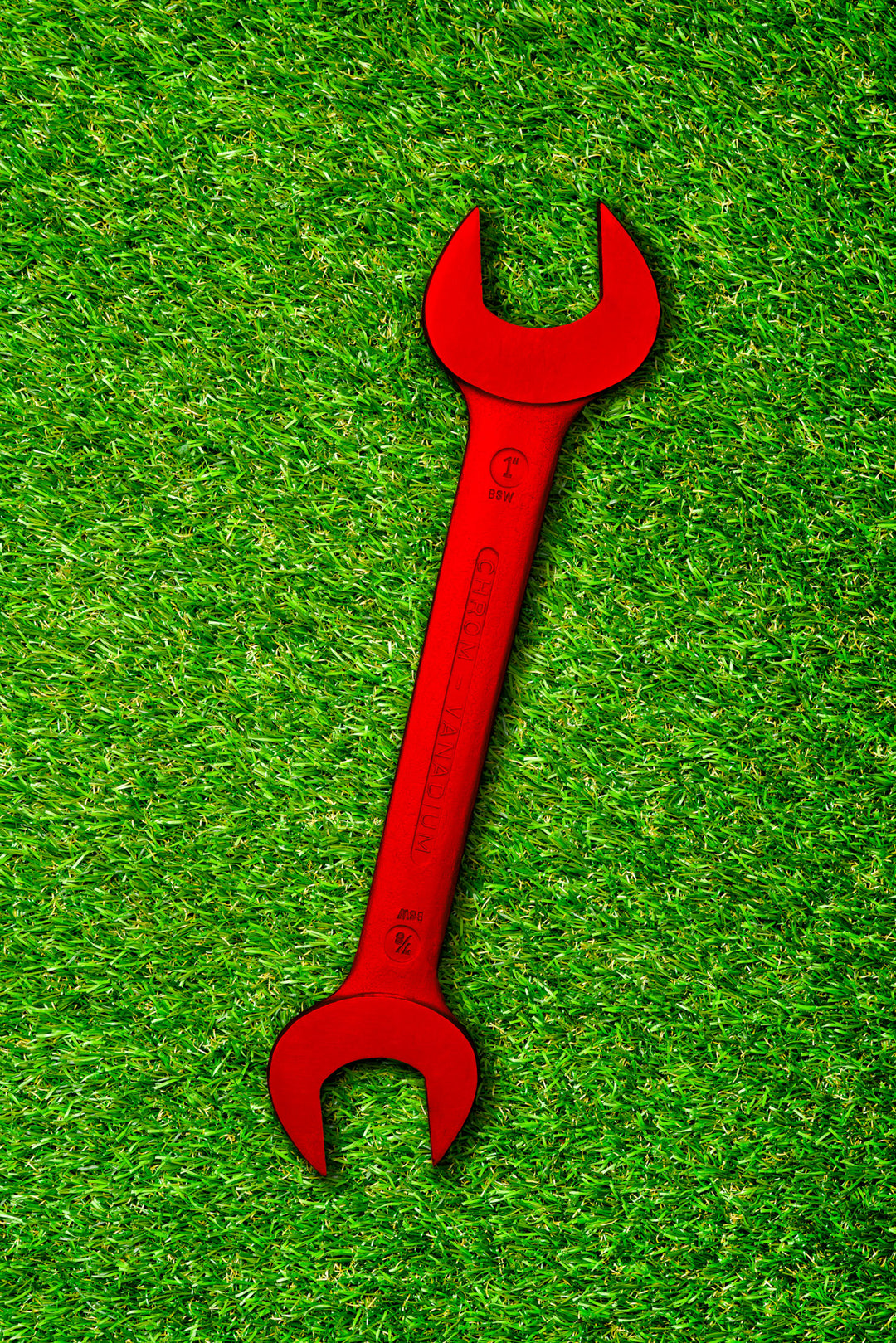 Bold red spanner placed diagonally on a vivid green grass background, creating a striking visual contrast.