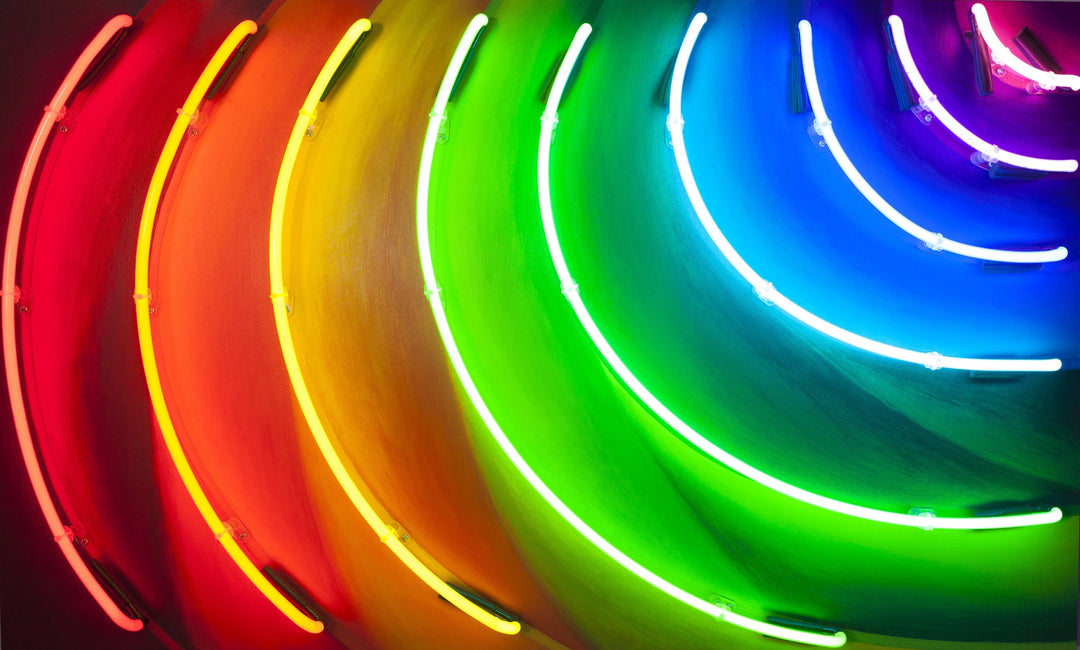 Curved neon light installation by Matthew Bracey forming a radiant spectrum across a wall, with glowing arcs in red, orange, yellow, green, blue, and violet. The light creates a dynamic rainbow effect that spills onto the surrounding surface, showcasing a bold and immersive colour experience.
