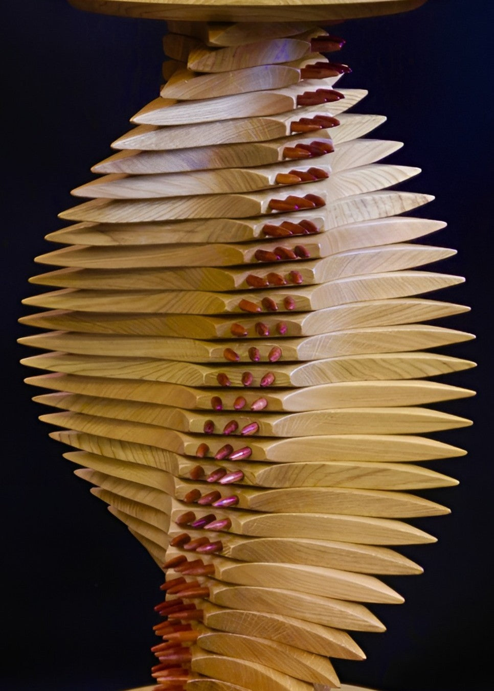 Sculptural oak and bubinga table with a twisting, spine-like form, its layered wooden structure punctuated by pointed red bubinga dowels that emphasise the gullet, creating rhythm, balance, and technorganic tension.