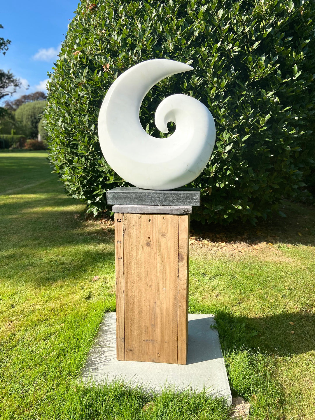 Spiral by Brendan Cullen, hand-carved from Statuario Marble, a smooth white sculpture in a curling spiral form with flowing curves and polished surface, mounted on a dark stone base.