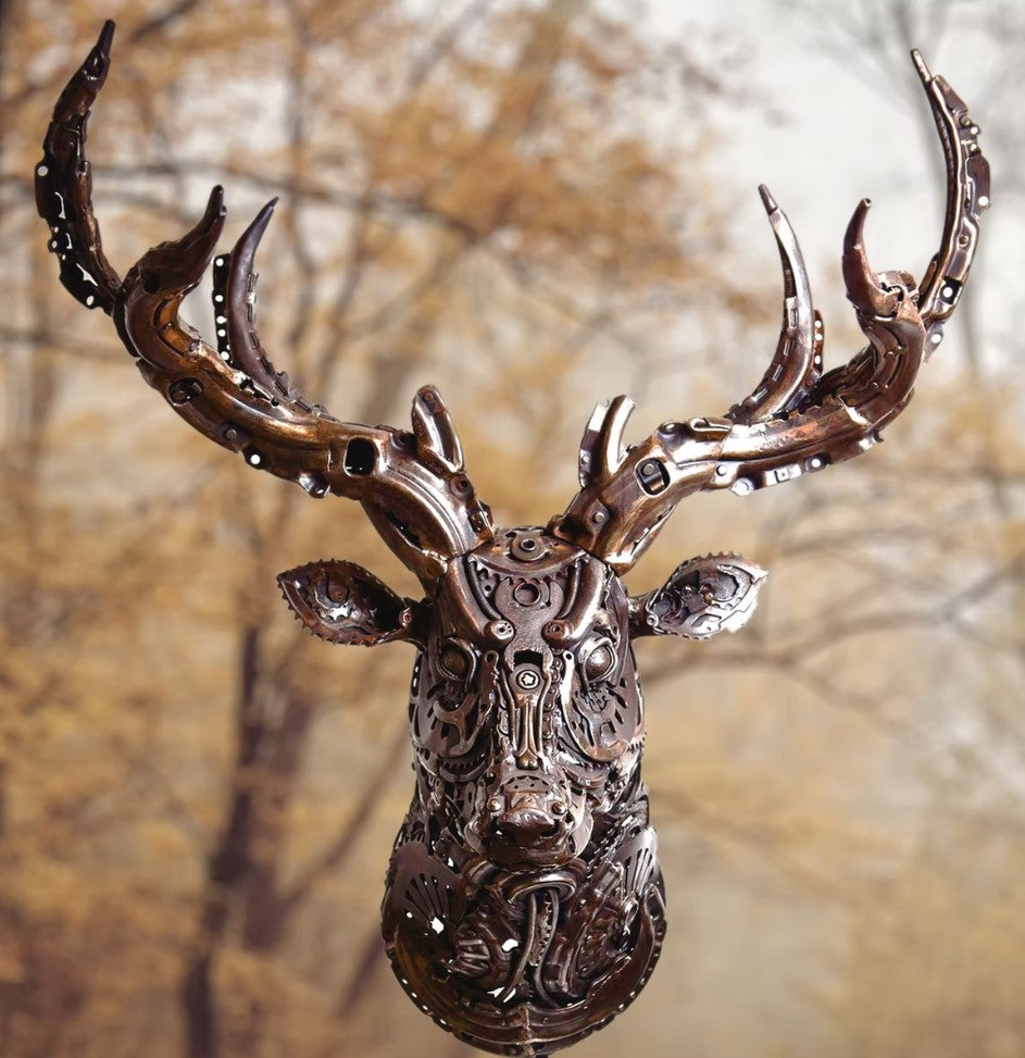 Sculpted stag head made from welded metal parts and gears, mounted against a white background.
