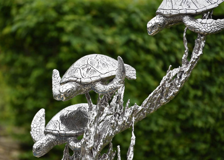‘Turtles Stainless Steel’ by Hamish Mackie, a limited-edition marine-grade stainless steel wildlife sculpture depicting three life-size sea turtles swimming through an intricate arrangement of underwater foliage. The polished silver-grey finish highlights the turtles' detailed shells, textured flippers and graceful movement, while the sweeping, branching forms create a sense of flowing water. Mounted on a rectangular stainless steel base, this contemporary sculpture is suitable for indoor or outdoor display