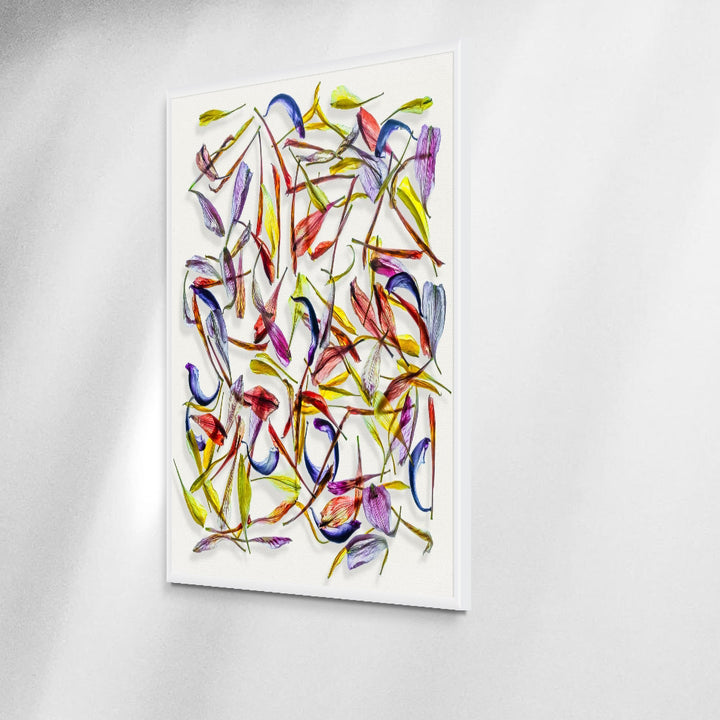 A meticulously arranged composition of vivid, translucent flower petals scattered across a clean white canvas. The petals display a rich palette of colours—reds, purples, blues, yellows, and greens—highlighting their fine textures and natural curves in a dynamic, layered pattern.