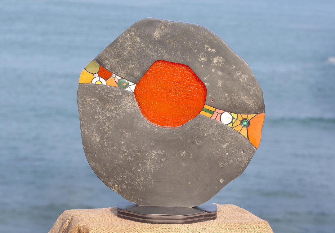 Slate and glass sculpture by Stacey Beaumont titled Sundancer, featuring reclaimed Delabole slate with a glowing amber-orange glass core, inlaid with sea-glass, fossils, ceramics, gemstones, and gold leaf, inspired by coastal light.