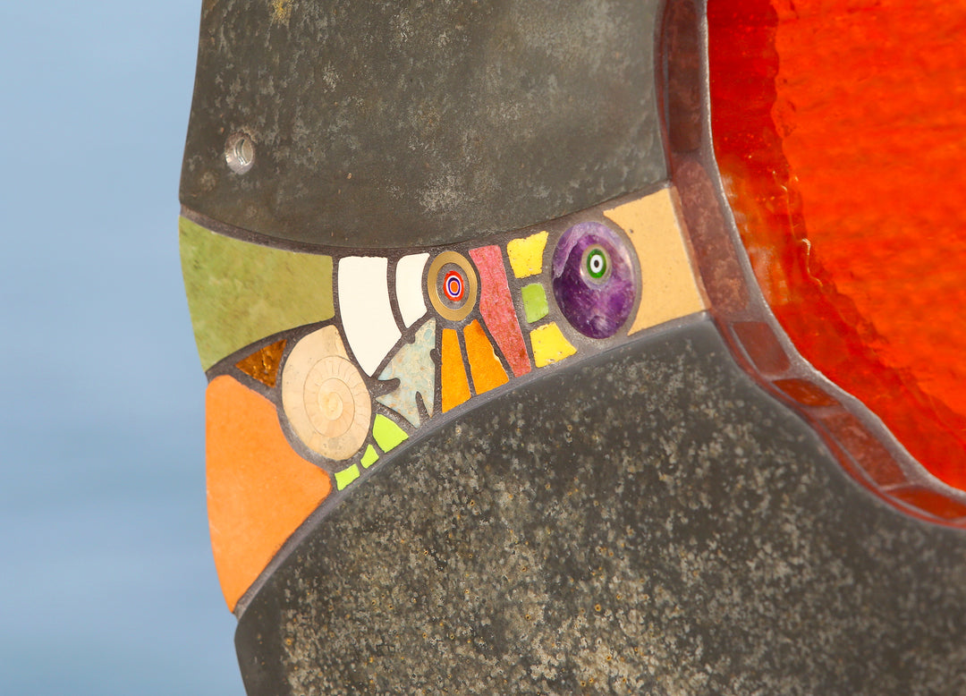 Slate and glass sculpture by Stacey Beaumont titled Sundancer, featuring reclaimed Delabole slate with a glowing amber-orange glass core, inlaid with sea-glass, fossils, ceramics, gemstones, and gold leaf, inspired by coastal light.