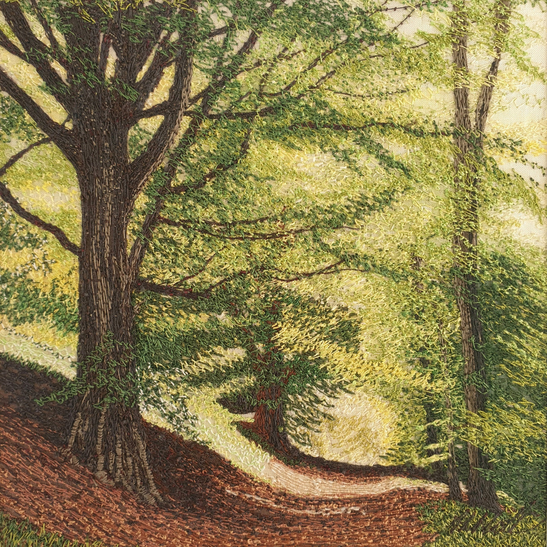 Intricately embroidered woodland scene with sunlit trees and a winding path through a leafy forest.


