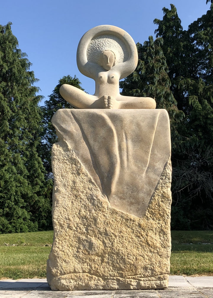 ‘Sunrise’ by Nicolas Moreton MRSS, a unique contemporary figurative stone sculpture carved from Ancaster Weatherbed Limestone, depicting a stylised seated female figure with crossed legs and raised arms forming a circular halo-like shape above her head. The figure features a delicately carved face, textured hair and smooth, rounded body, emerging from a large rectangular limestone block with a rough natural surface and flowing carved folds. Finished in warm cream, pale beige and natural limestone tones, the