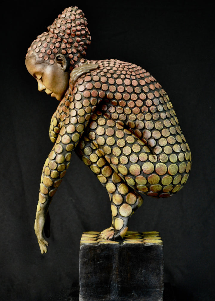 Bronze sculpture of a crouching female figure, her body covered in a gradual pattern of circular, sunset-toned discs that shift from warm reds to soft golds. She balances on a textured block, head bowed gently in a contemplative pose, with a dark backdrop emphasising the warmth and depth of the patina.