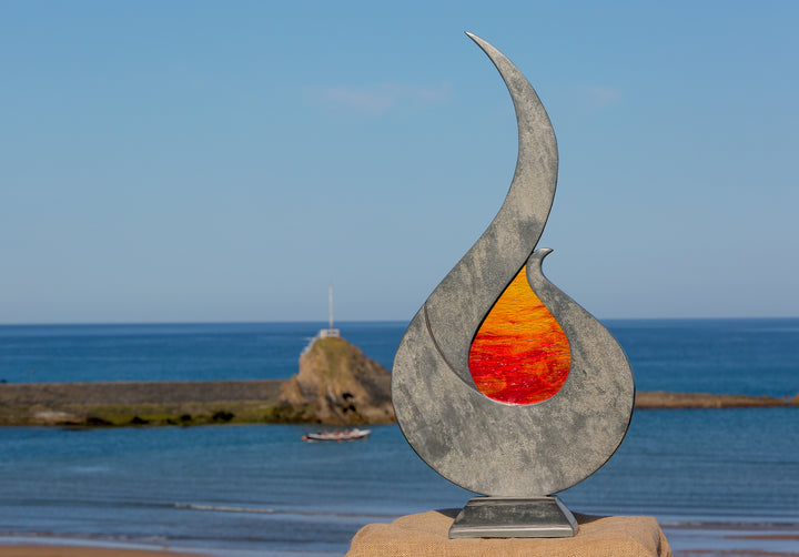 Stacey Beaumont Sunstone slate and glass sculpture, a flame-like form in reclaimed Delabole slate with textured orange and red glass centre inspired by Atlantic sunsets.
