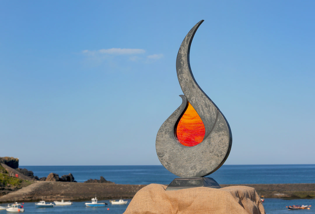 Stacey Beaumont Sunstone slate and glass sculpture, a flame-like form in reclaimed Delabole slate with textured orange and red glass centre inspired by Atlantic sunsets.