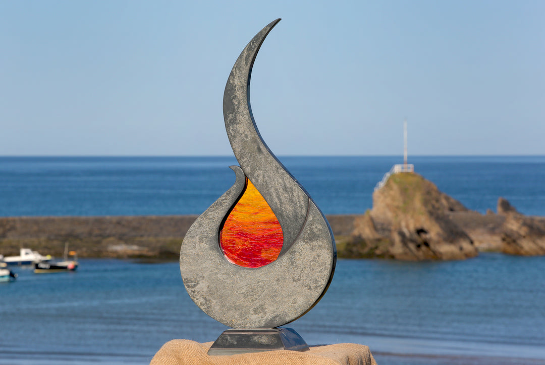 Stacey Beaumont Sunstone slate and glass sculpture, a flame-like form in reclaimed Delabole slate with textured orange and red glass centre inspired by Atlantic sunsets.