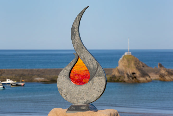 Stacey Beaumont Sunstone slate and glass sculpture, a flame-like form in reclaimed Delabole slate with textured orange and red glass centre inspired by Atlantic sunsets.