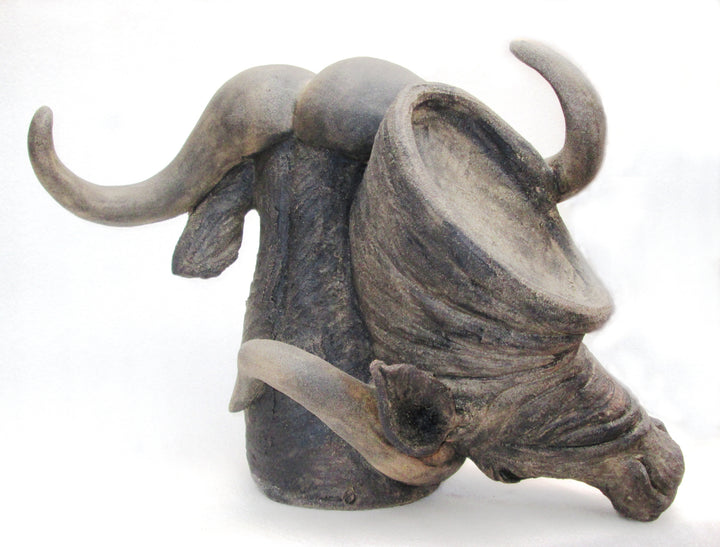 Sculptural ceramic of two buffalo heads intertwined, crafted in textured stoneware with naturalistic detail and expressive curvature. One head faces forward while the other tilts downward, their horns looping in dynamic, sculptural tension against a neutral background.