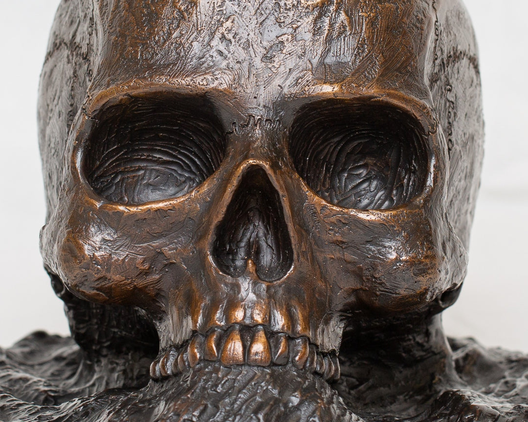 Remember Death bronze skull sculpture by Tom Saxton emerging from textured bronze ground, detailed human skull memento mori sculpture in rich dark bronze, warm copper-brown tones and deep shadowed cavities, contemporary philosophical bronze artwork